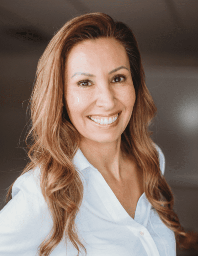 Darla stands smiling in a boardroom wearing a white button-up shirt.